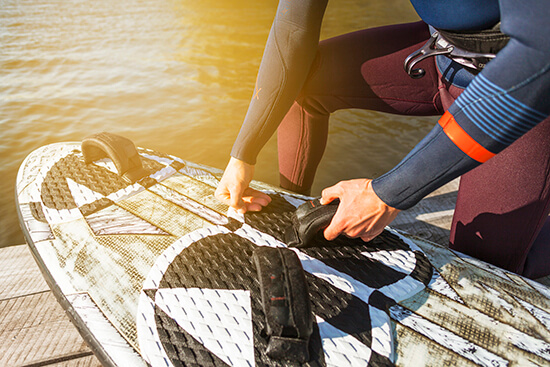 Person securing a wakeboard on a dock beside the water before watersports activity